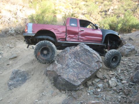 1985 Toyota 4Runner - Pickup truck with significant body damage and aftermarket suspension on a rock obstacle.
