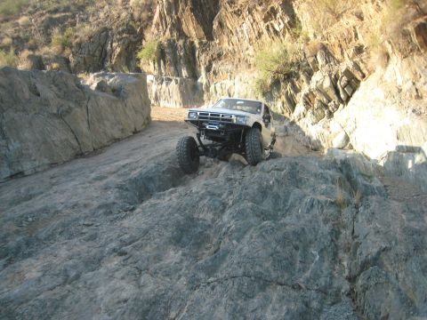 1985 Toyota 4Runner - A modified white SUV navigates a challenging rocky trail in a canyon.