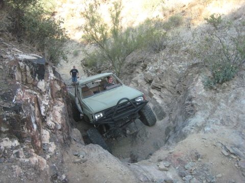 1985 Toyota 4Runner - A light green Toyota pickup truck navigates a challenging rocky off-road trail, demonstrating its capability on difficult terrain.