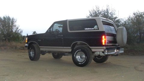 1996 Ford Bronco - This 1996 Ford Bronco is shown from the rear, parked on a dirt road with trees in the background.