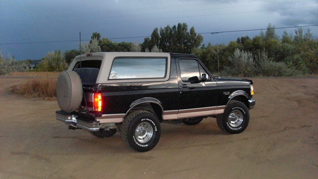 Black and tan Ford Bronco with spare tire carrier, 3/4 rear view on dirt lot