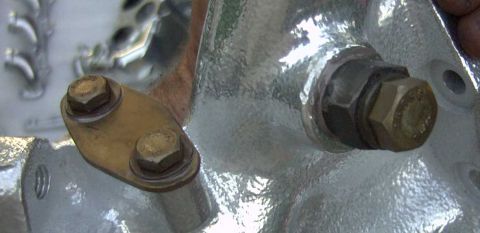 1997 Ford Taurus - Close-up of a metallic silver exhaust manifold or cylinder head casting with a mustard-yellow block-off plate secured by two hex bolts with…