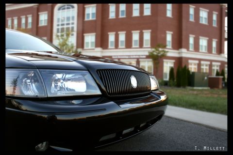 2003 Mercury Marauder - Close-up of a black 2003 Mercury Marauder's grille and headlights with a brick building in the background.