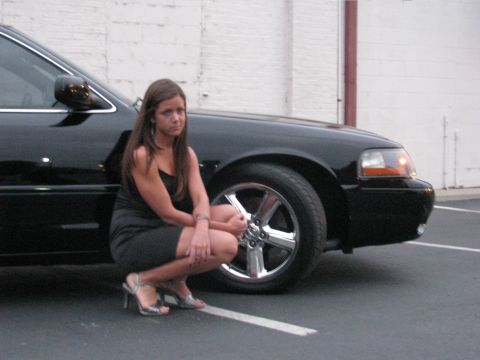 2003 Mercury Marauder - A woman in a black dress crouches beside a black 2003 Mercury Marauder.