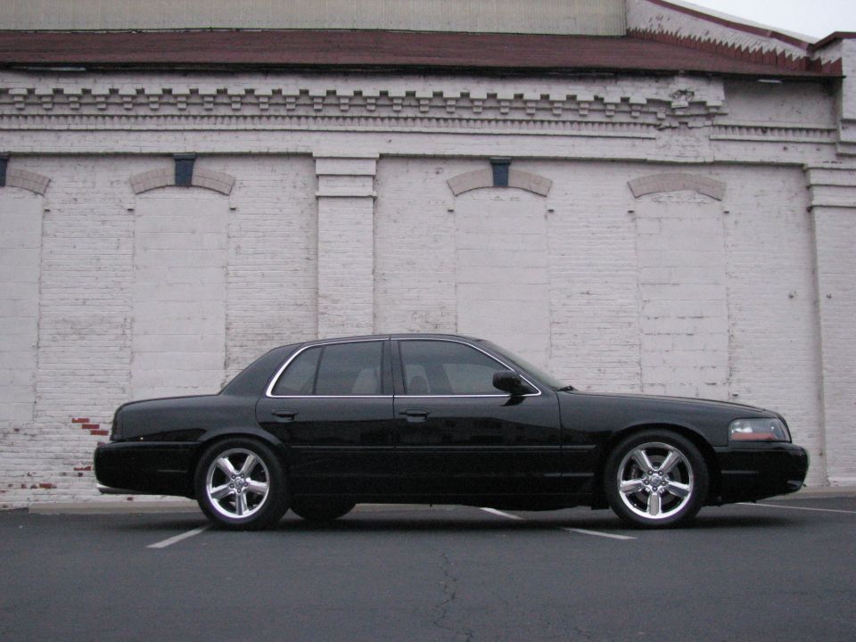 Black Mercury Marauder sedan on chrome wheels by a white brick wall