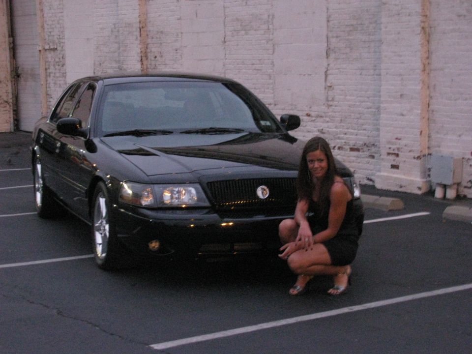 Black 2003 Mercury Marauder parked in a lot with a woman crouching in front of the grille