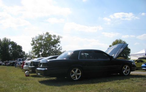 2003 Mercury Marauder - Several cars are lined up on a grassy field under a clear sky, with one car's hood open.