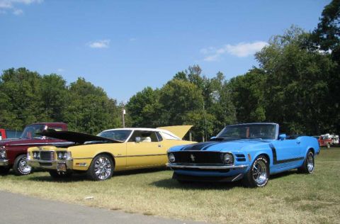 2003 Mercury Marauder - A blue convertible muscle car with black racing stripes is parked on a grassy field under a clear blue sky.