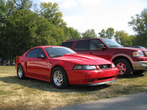 2003 Mercury Marauder - A red Ford Mustang with a hood scoop and drag racing tires is parked on grass next to a red SUV.
