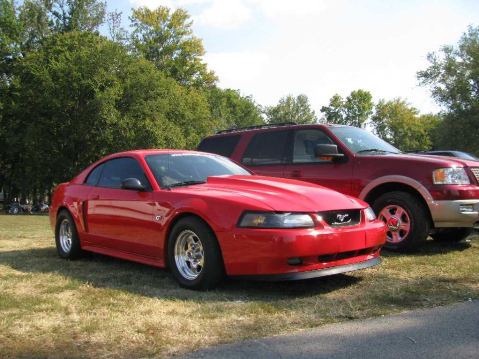 Red Ford Mustang with hood scoop and drag tires parked next to a red SUV