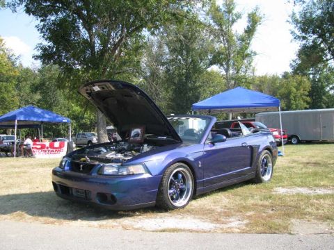 2003 Mercury Marauder - A blue convertible sports car with its hood open is parked on a grassy field near tents and a trailer.