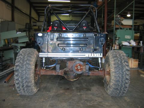 1992 Ford Mustang - The rear of a modified Jeep Wrangler is shown in a workshop setting, a roll cage and large tires.