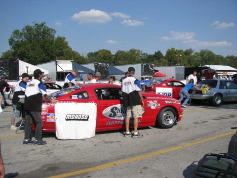 2003 Mercury Marauder - A red race car with "Moroso" and "Sutton High Performance" logos is parked at a track event, with other vehicles and people around.