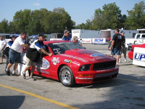 2003 Mercury Marauder - A red Ford Mustang drag car is being pushed by several people at a race track.