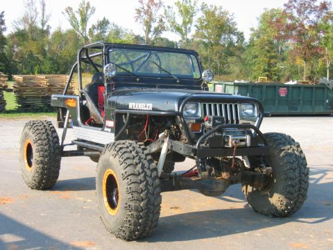 1992 Ford Mustang - Modified black Jeep Wrangler with prominent roll cage and oversized tires sits outdoors.