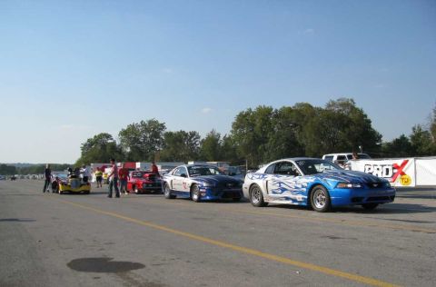 2003 Mercury Marauder - Drag cars lined up on a track with spectators and other vehicles present under a clear blue sky.