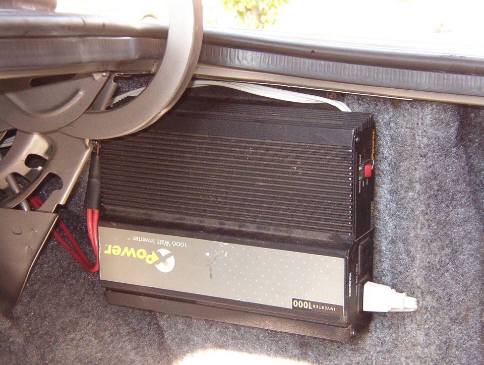 Black 1000-watt power inverter mounted in carpeted vehicle trunk