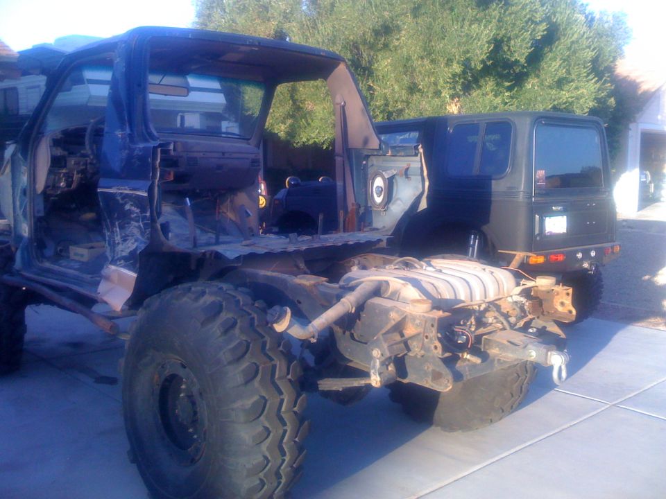 stripped-down vehicle chassis with large tires, another vehicle body behind it