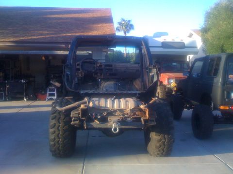 1994 Ford Bronco - This heavily modified SUV chassis, viewed from the rear, features large off-road tires and an exposed frame, with another vehicle partially…