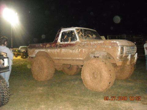 1979 Ford Bronco - This heavily mud-caked 1979 Ford Bronco is shown from a three-quarter front angle at an outdoor event.