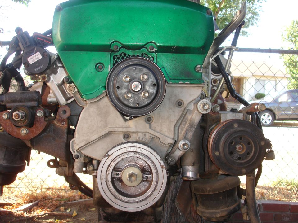 Green engine block with pulleys and hoses, viewed from the front