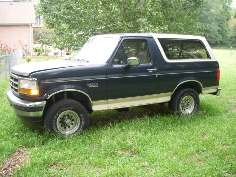 1993 Ford Bronco - This Ford Bronco is parked on a grassy lawn in front of a house and trees.
