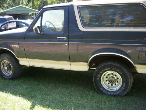1993 Ford Bronco - This Ford Bronco is parked on grass with another vehicle and a building in the background.