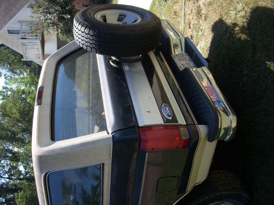 Rear of a two-tone green and tan Ford Bronco with tailgate spare tire, parked on grass; image rotated sideways.