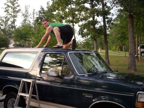 1993 Ford Bronco - Man on top of a dark green 1993 Ford Bronco, with a ladder positioned next to the vehicle.