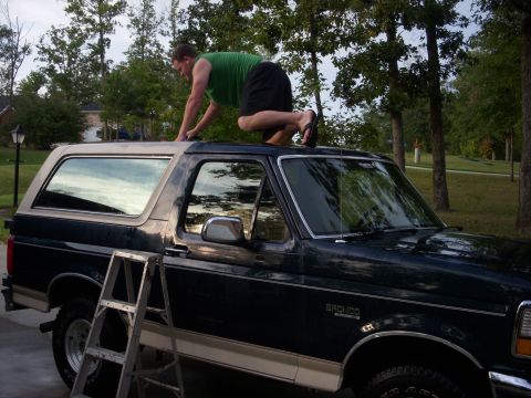 1993 Ford Bronco - A man is cleaning the roof of a dark green Ford Bronco with a tan top. A ladder is placed beside the vehicle.