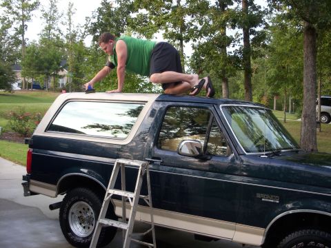 1993 Ford Bronco - Man cleans the roof of a dark green and tan SUV, with a ladder positioned for access.