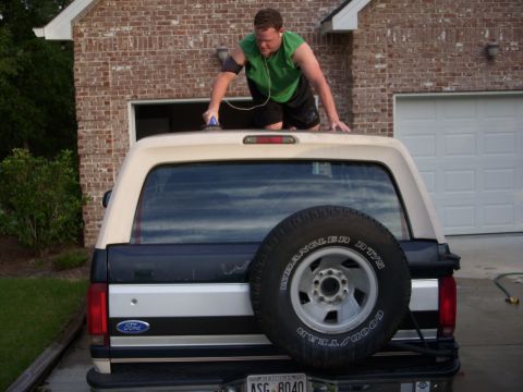 1993 Ford Bronco - A man is on the roof of a 1993 Ford Bronco, cleaning it before putting it in the garage.