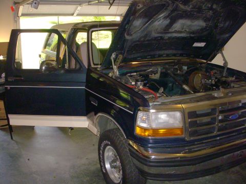 1993 Ford Bronco - The 1993 Ford Bronco's engine is exposed with the hood open and driver's door ajar.