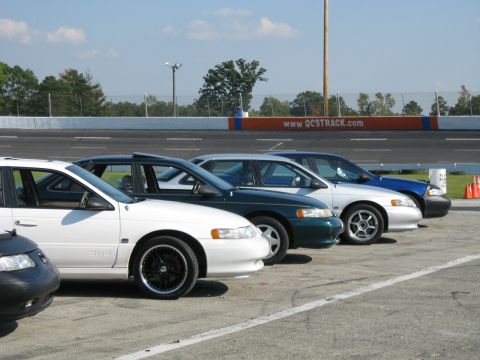 1993 Ford Taurus - Multiple sedans are parked in a row next to a racing track.