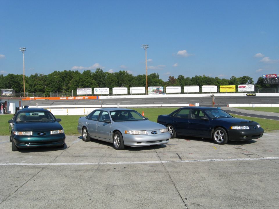 Three 1993 Ford Taurus sedans parked in front of a racetrack