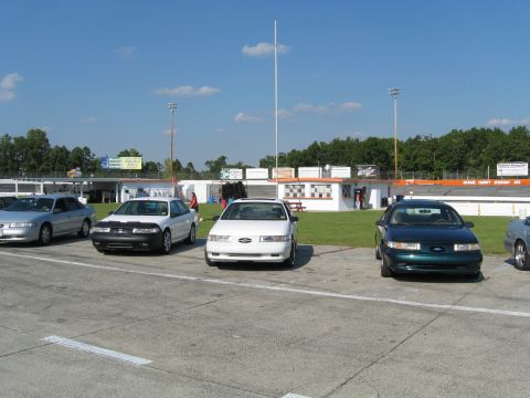 1993 Ford Taurus - Several sedans are parked at a racetrack on a sunny day.