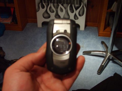 1995 Ford Bronco - A flip phone with a digital display is held in a hand, with a decorative flame pattern in the background.