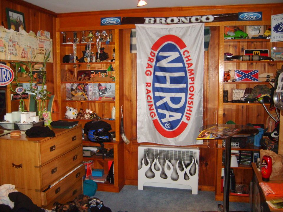 Room decorated with Ford and Bronco signs, NHRA flag, and trophies