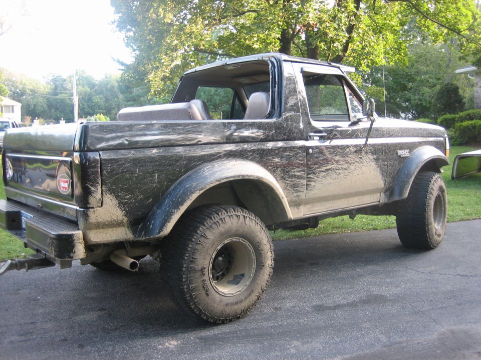 Black Ford Bronco covered in mud, rear quarter view, with removable top