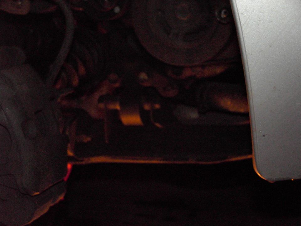 Undercarriage of a vehicle showing brake caliper, suspension components, and engine belt system