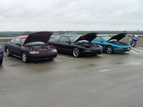 1989 Ford Probe - Three Ford Probes are parked side-by-side with their hoods open, a motorcycle is parked nearby.