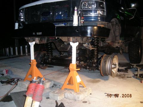 1993 Ford Bronco - The front end of a Ford truck is elevated on jack stands, undergoing maintenance with the wheels off.