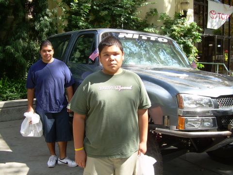 1986 Ford Bronco - Two people stand in front of a gray SUV with a custom bumper and a Nitto banner on the windshield.