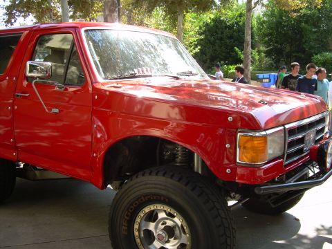 1986 Ford Bronco - This red 1986 Ford Bronco features a lifted suspension, aftermarket wheels, and a custom front bumper.