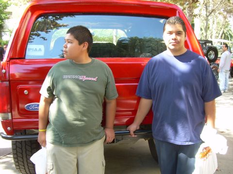 1986 Ford Bronco - A red 1986 Ford Bronco is seen from the rear with two individuals posing beside it.