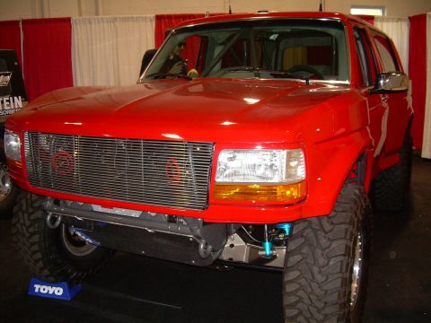 1986 Ford Bronco - This red Ford Bronco features a custom grille, aftermarket suspension, and a roll cage, suggesting a later model year than 1986.