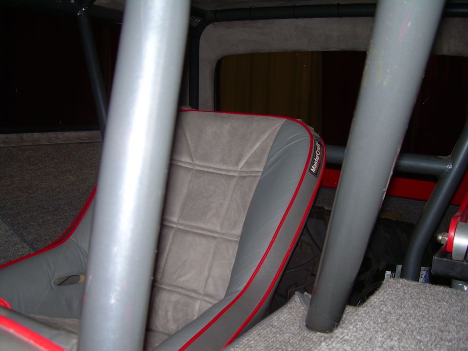 Gray racing seat with red trim inside a vehicle with a roll cage