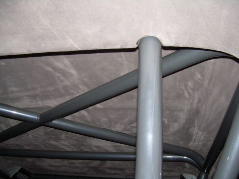 1986 Ford Bronco - The interior of a vehicle shows a custom roll cage structure against a gray headliner.