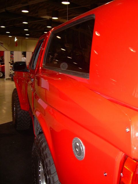 1986 Ford Bronco - This red SUV, likely from the 1980s, is shown from the side with large off-road tires and a visible fuel cap.