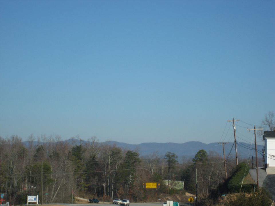 Two white sedans and a black sedan on a highway with mountains in the background